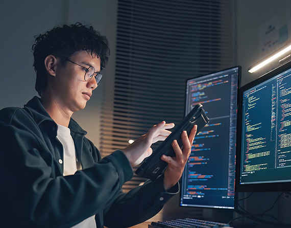 Pessoa trabalhando na frente de computadores e com tablet na mão